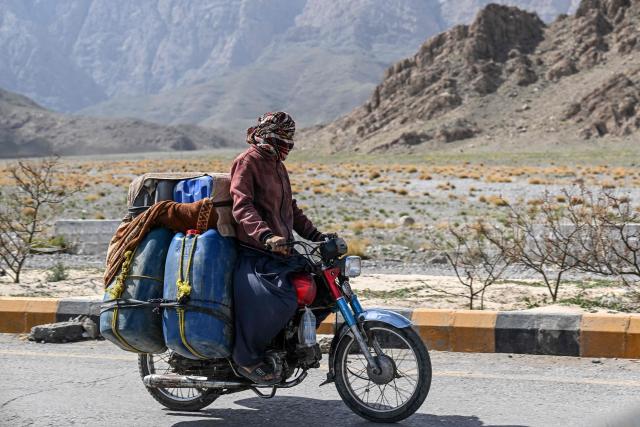 This photograph taken on March 14, 2026 shows a vendor transporting jerrycans filled with smuggled Iranian petrol on his motorcycle, on the outskirts of Quetta in Balochistan province. (Photo by Banaras KHAN / AFP)