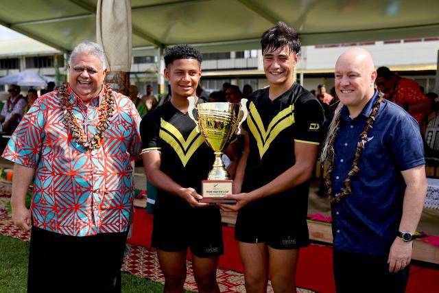 New Zealand’s Prime Minister Christopher Luxon (R) and his Samoan counterpart La'aulialemalietoa Leuatea Schmidt (L) pose for photos with players from the winning Tipene College rugby team from Auckland after their Prime Minister’s Cup match against Samoa’s Wesley College in the village of Faleula, Samoa, on March 17, 2026. (Photo by Ben STRANG / AFP)