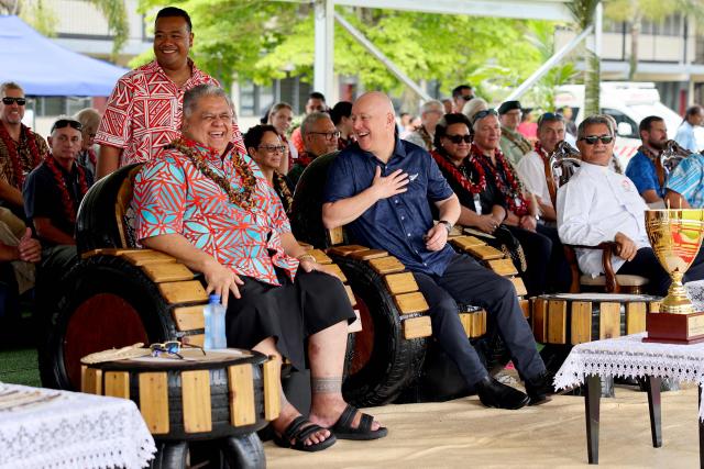 New Zealand’s Prime Minister Christopher Luxon (C) and his Samoan counterpart La'aulialemalietoa Leuatea Schmidt (L) watch the rugby match between Tipene College from Auckland and Samoa’s Wesley College in the village of Faleula, Samoa, on March 17, 2026. (Photo by Ben STRANG / AFP)