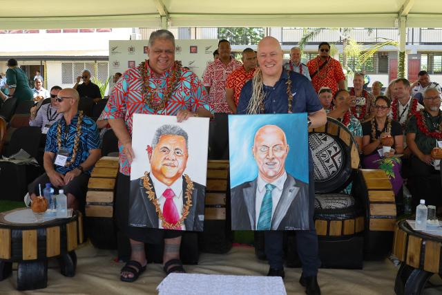 New Zealand’s Prime Minister Christopher Luxon (R) and his Samoan counterpart La'aulialemalietoa Leuatea Schmidt display portraits presented to them by an artist during the rugby match between Auckland’s Tipene College and Samoa’s Wesley College in the village of Faleula, Samoa, on March 17, 2026. (Photo by Ben STRANG / AFP)