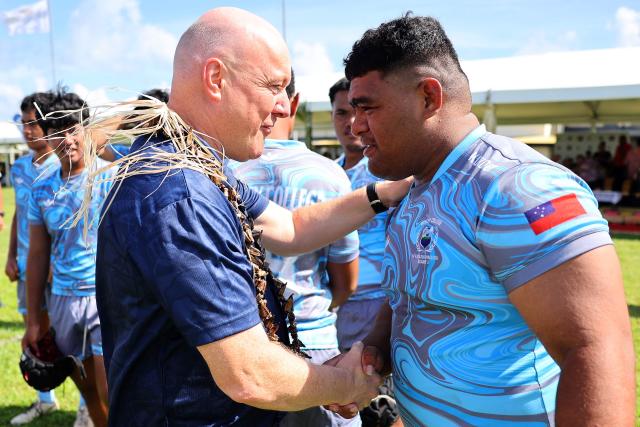 New Zealand's Prime Minister Christopher Luxon (L) greets a player from Samoa’s Wesley College player before their rugby match against Auckland’s Tipene College in the village of Faleula, Samoa, on March 17, 2026. (Photo by Ben STRANG / AFP)