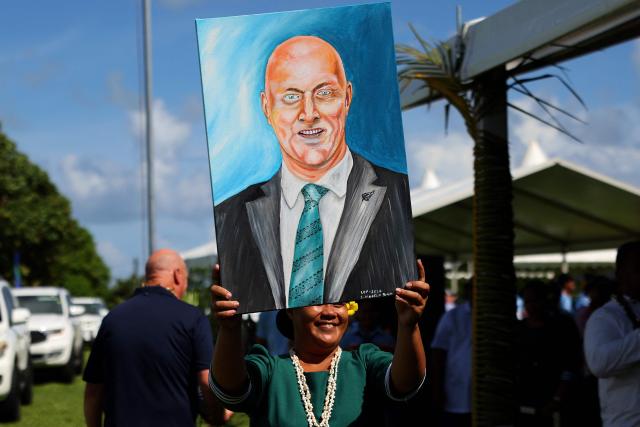 A woman carries a portrait of New Zealand’s Prime Minister Christopher Luxon during the Prime Ministers Cup rugby match between Samoa’s Wesley College and Auckland’s Tipene College in the village of Faleula, Samoa, on March 17, 2026. (Photo by Ben STRANG / AFP)