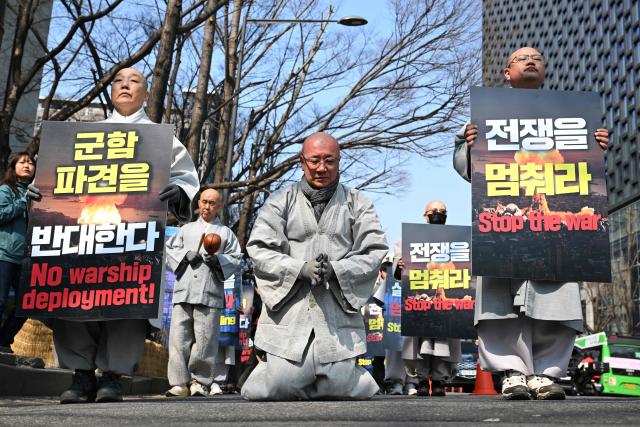 South Korean Buddhist monks perform full bows as they march towards the US embassy during a protest against the war on Iran in Seoul on March 17, 2026. (Photo by Jung Yeon-je / AFP)
