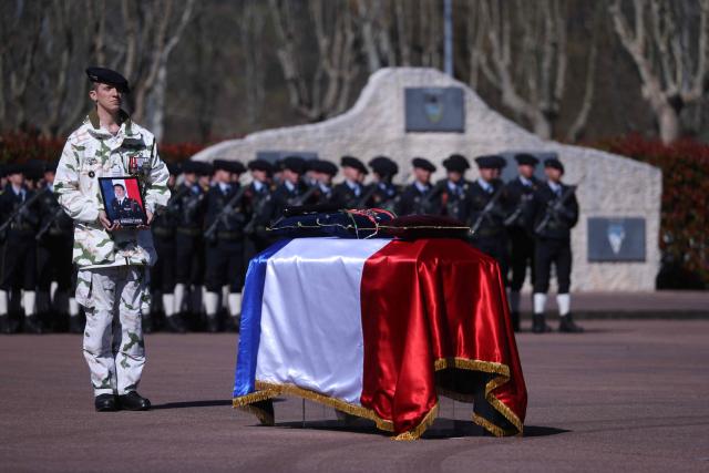 A French soldier of "Troupes de montagne" of Chasseurs Alpins (Alpine Hunters) holds a portrait in front of the coffin of Chief Warrant Officer Arnaud Frion who was killed in a drone attack in Erbil on March 12, 2026, during a national tribute ceremony at the 7th Alpine Chasseurs Battalion in Varces, southeastern France on March 17, 2026. Arnaud Frion was killed and six other French soldiers were wounded on March 12, 2026 evening in a drone attack in the Erbil region of Iraqi Kurdistan, French authorities announced, lamenting the first death within the French army in the context of the war in the Middle East. (Photo by Alex MARTIN / AFP)