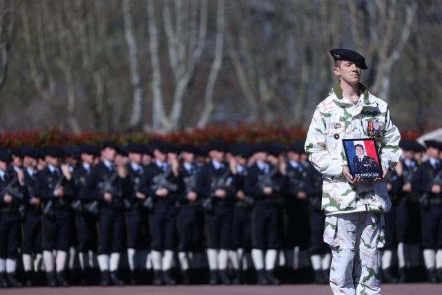 A French soldier of "Troupes de montagne" of Chasseurs Alpins (Alpine Hunters) holds a portrait in front of the coffin of Chief Warrant Officer Arnaud Frion who was killed in a drone attack in Erbil on March 12, 2026, during a national tribute ceremony at the 7th Alpine Chasseurs Battalion in Varces, southeastern France on March 17, 2026. Arnaud Frion was killed and six other French soldiers were wounded on March 12, 2026 evening in a drone attack in the Erbil region of Iraqi Kurdistan, French authorities announced, lamenting the first death within the French army in the context of the war in the Middle East. (Photo by Alex MARTIN / AFP)