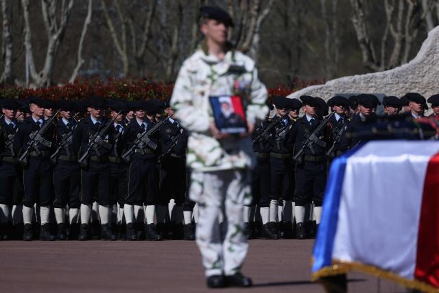A French soldier of "Troupes de montagne" of Chasseurs Alpins (Alpine Hunters) holds a portrait in front of the coffin of Chief Warrant Officer Arnaud Frion who was killed in a drone attack in Erbil on March 12, 2026, during a national tribute ceremony at the 7th Alpine Chasseurs Battalion in Varces, southeastern France on March 17, 2026. Arnaud Frion was killed and six other French soldiers were wounded on March 12, 2026 evening in a drone attack in the Erbil region of Iraqi Kurdistan, French authorities announced, lamenting the first death within the French army in the context of the war in the Middle East. (Photo by Alex MARTIN / AFP)