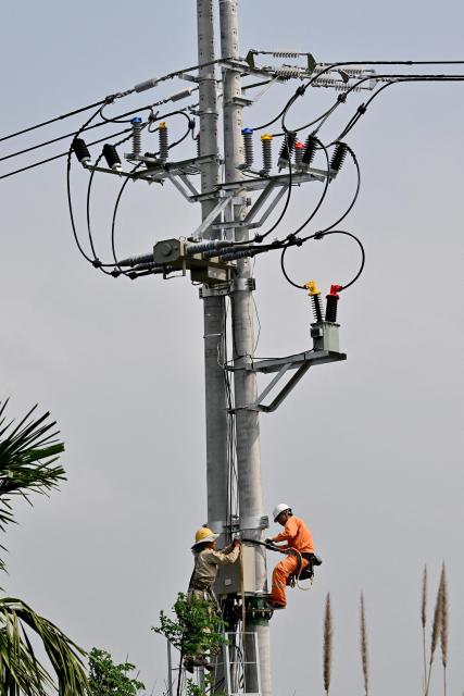Electricians work on a transmission pole at a construction site in Hanoi on March 17, 2026. (Photo by Nhac NGUYEN / AFP)