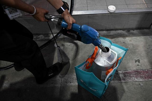 An employee fills a motorist's container at a Caltex petrol station in the northern Thai province of Chiang Rai on March 17, 2026, following import disruptions caused by the Middle East war. Oil prices rose again on March 17 as Iran launched fresh attacks on crude-producing neighbours, while stock markets were higher ahead of key central bank meetings. (Photo by Lillian SUWANRUMPHA / AFP)
