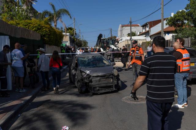 Members of the security forces, municipality officials and residents gather next to the wreckage of a car at the site of a strike in Rishon LeZion, on the outskirts of Tel Aviv, on March 17, 2026. On February 28, 2026, Israel and the United States launched strikes on Iran, killing its supreme leader and triggering a war that spread across the Middle East. (Photo by Ilia YEFIMOVICH / AFP) / 