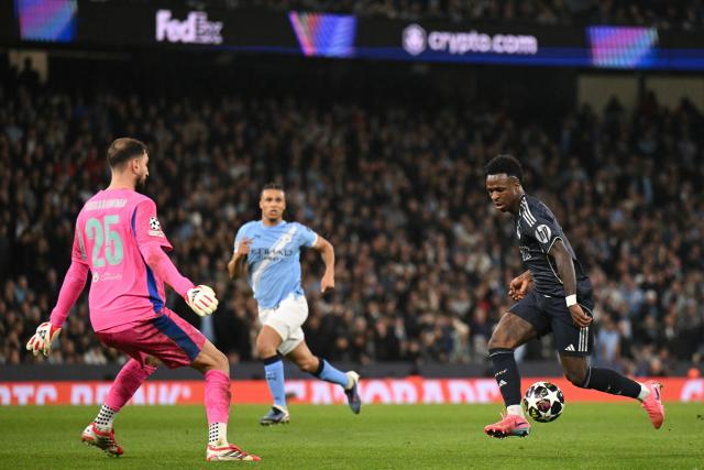 Real Madrid's Brazilian forward #07 Vinicius Junior (R) collides with Manchester City's Italian goalkeeper #25 Gianluigi Donnarumma (L) as he runs in on goal during the UEFA Champions League, round of 16 second leg football match between Manchester City and Real Madrid at the Etihad Stadium in Manchester, north west England, on March 17, 2026. (Photo by Oli SCARFF / AFP)