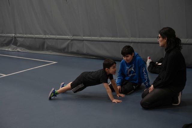 A Greenlandic child imitates push ups in front of his mother and brother during a boxing training session in Nuuk, Greenland, on March 4, 2026. Greenland has one of the highest suicide rates in the world, especially among teenagers and young adults. Psychiatric care is uneven, and many youths must leave their families to study in Nuuk. In the capital, many turn to boxing as a way to channel their pain. (Photo by Florent VERGNES / AFP)