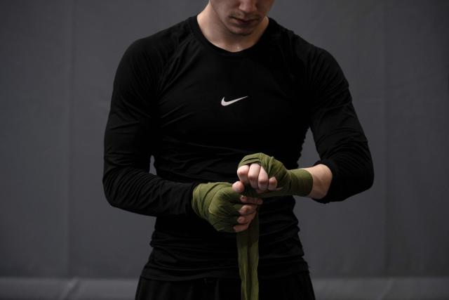 Kian, 19, young Greenlandic boxer, wraps his hands with gauze bandages before a training session at the Nuuk stadium, in Greenland, on March 4, 2026. Greenland has one of the highest suicide rates in the world, especially among teenagers and young adults. Psychiatric care is uneven, and many youths must leave their families to study in Nuuk. In the capital, many turn to boxing as a way to channel their pain. (Photo by Florent VERGNES / AFP)