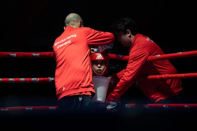 A boy from the club has water poured over his head during a break in a boxing match in Nuuk, Greenland, on February 28, 2026. Greenland has one of the highest suicide rates in the world, especially among teenagers and young adults. Psychiatric care is uneven, and many youths must leave their families to study in Nuuk. In the capital, many turn to boxing as a way to channel their pain. (Photo by Florent VERGNES / AFP)