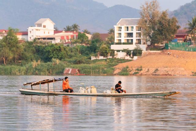 A man and a child travel by boat carrying sacks of goods along the Mekong river in Luang Prabang on March 16, 2026. (Photo by AFP)