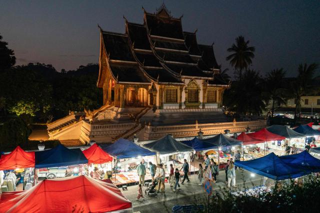 Visitors walk past a temple through a night market in Luang Prabang on March 16, 2026. (Photo by AFP)