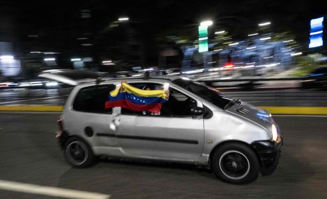 A Venezuela fan waves a national flag from a car window as they celebrate their national baseball team's victory in the final of the 2026 World Baseball Classic against the United States team, in Caracas on March 17, 2026. Venezuela, where baseball is the national sport, capped off its dream tournament by defeating the favorite, the United States, on home soil, amid tense relations between the two governments following the capture of President Nicolas Maduro by US forces in January. (Photo by Juan BARRETO / AFP)