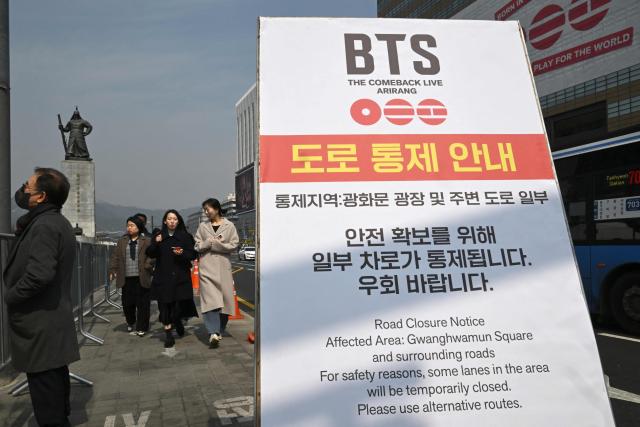 This picture taken on March 16, 2026 shows pedestrians passing a road closure notice for a comeback concert of K-pop boy group BTS at Gwanghwamun Square in Seoul. More than a quarter of a million fans are expected to throng central Seoul on March 21 for BTS's open-air gig, the first performance in almost four years by the boy band seen as the biggest in the world. (Photo by Jung Yeon-je / AFP)