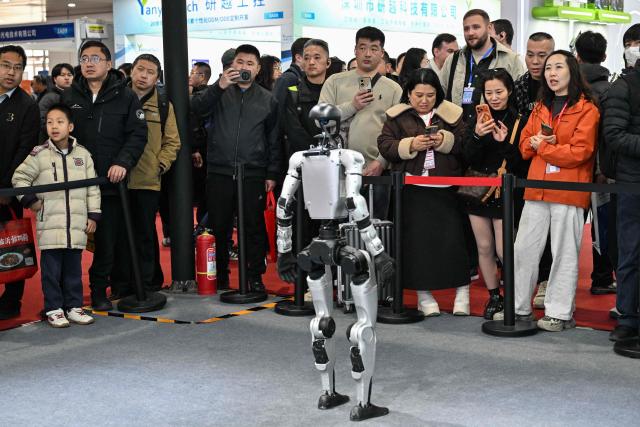 Visitors watch a Unitree humanoid robot during the International AI Application and Robotics Innovation Exhibition in Beijing on March 18, 2026. (Photo by ADEK BERRY / AFP)