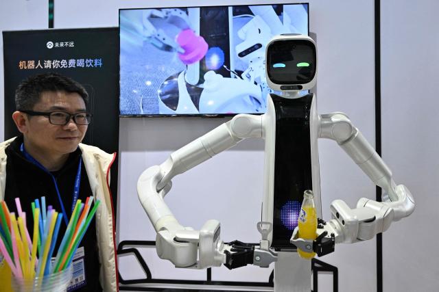 A man stands next to a robot during the International AI Application and Robotics Innovation Exhibition in Beijing on March 18, 2026. (Photo by ADEK BERRY / AFP)