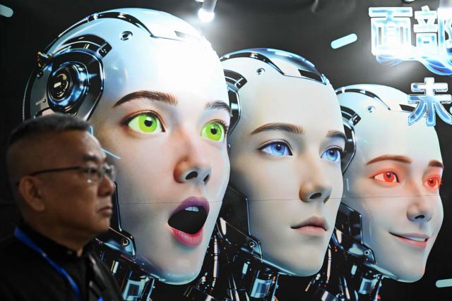A man stands next to a poster showing robots mimicking human expressions from Shenzhen Xiaoquan Technology during the International AI Application and Robotics Innovation Exhibition in Beijing on March 18, 2026. (Photo by ADEK BERRY / AFP)