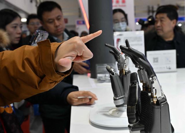 People check bionic hands from Yuequan Bionics during the International AI Application and Robotics Innovation Exhibition in Beijing on March 18, 2026. (Photo by ADEK BERRY / AFP)