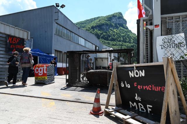(FILES) Workers on strike to protest against a social plan walk past placards reading "No to the closure of MBF" at the entrance of the MBF aluminum foundry plant in Saint-Claude, northeastern France on June 10, 2021. A three-year suspended prison sentence and a Ђ300,000 fine were requested on March 17, 2026 in Nancy against the former head of a Jura-based automotive supplier, prosecuted for embezzling Ђ9 million from the company's treasury before its liquidation in 2021, leaving nearly 300 employees jobless. Gianpiero Colla, 64, former head of the MBF Aluminium automotive foundry in Saint-Claude (Jura), is on trial for "misuse of company assets" and "presenting inaccurate annual accounts." (Photo by PHILIPPE DESMAZES / AFP)