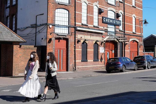 Pedestrians (L) wearing face masks walk past Club Chemistry (R), a nightclub linked to a recent outbreak of meningitis in Canterbury, south-east England on March 18, 2026. The number of meningitis cases being probed by UK authorities has risen to 20, health officials said on March 18, following an "unprecedented" deadly outbreak centred on a university. The outbreak in Kent in southeastern England has claimed the lives of two young people -- a 21-year-old university student and an 18-year-old school student. (Photo by CARLOS JASSO / AFP)