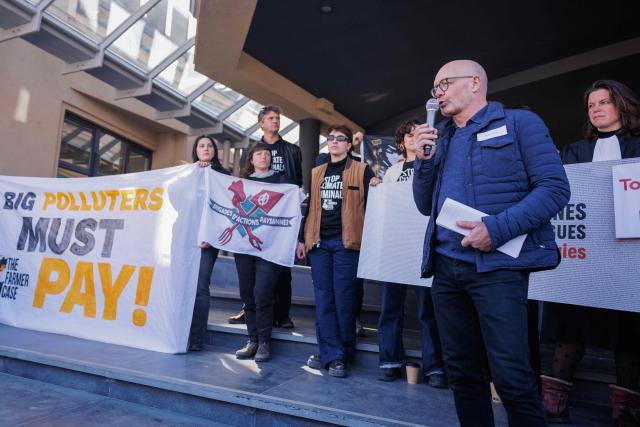 Belgian farmer Hugues Falys delivers a speech next to a banner reading "Polluters must pay" before the verdict in the climate court case, in which he seeks compensation from French oil giant TotalEnergies for damage to his farm caused by climate change, in Tournai, on March 18, 2025. Several groups and a Belgian farmer asked the court to order TotalEnergies to reduce its oil and gas production to "ease the existential anxiety" linked to climate change. (Photo by Simon Wohlfahrt / AFP)