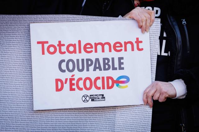 An NGO activist holds a sign reading "totally guilty of Ecocide" before the verdict in the climate court case, in which he seeks compensation from French oil giant Total Energies for damage to his farm caused by climate change, in Tournai, on March 18, 2025. Several groups and a Belgian farmer asked the court to order TotalEnergies to reduce its oil and gas production to "ease the existential anxiety" linked to climate change. (Photo by Simon Wohlfahrt / AFP)