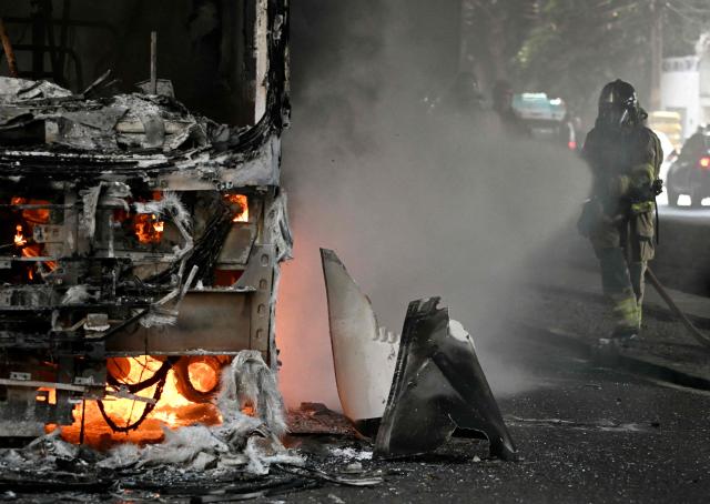 Firefighters work to put out a fire on a bus allegedly set by drug traffickers with home extinguishers during a police operation in central Rio de Janeiro, Brazil, on March 18, 2026. (Photo by Mauro PIMENTEL / AFP)
