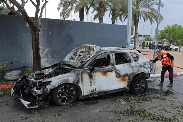 An Israeli first responder inspects the site of an Iranian strike that hit a car in Petah Tikva on March 18, 2026. On February 28, Israel and the United States launched strikes on Iran, killing its supreme leader Ayatollah and triggering a war that spread across the Middle East. (Photo by Jack GUEZ / AFP) / 