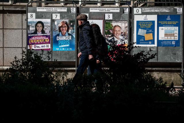 A person walks by campaign posters of the three remaining candidates for Paris mayor (From L) leftist Sophia Chikirou, right-wing Rachida Dati and socialist Emmanuel Gregoire, outside a poling station in Paris' 14th arrondissement, four days ahead of France's municipal elections second round, on March 18, 2026. (Photo by Guillaume BAPTISTE / AFP)