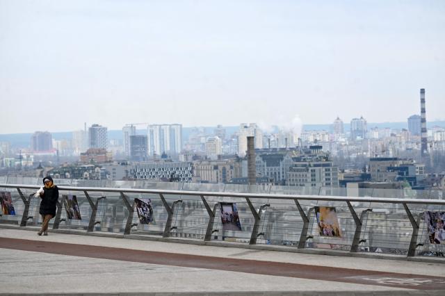 A girl holds a pigeon as she stands in front of Kyiv view on a cold spring day on March 18, 2026 amid the Russian invasion in Ukraine. (Photo by Sergei SUPINSKY / AFP)