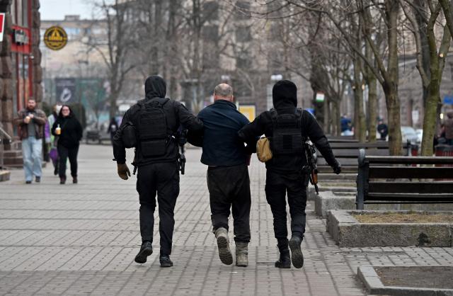 Police officers escort an unknown person they detained in the center of Kyiv on March 18, 2026, amid the Russian invasion in Ukraine. (Photo by Sergei SUPINSKY / AFP)