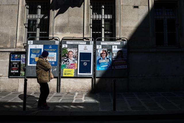 A person watches campaign posters of the three remaining candidates for Paris mayor (From L) socialist Emmanuel Gregoire, right-wing Rachida Dati and leftist Sophia Chikirou, outside Paris' 7th arrondissement city hall, four days ahead of France's municipal elections second round, in Paris on March 18, 2026. (Photo by Guillaume BAPTISTE / AFP)