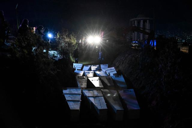 TOPSHOT - Afghan volunteers place coffins of victims who were killed in a Pakistani air strike on a drug rehabilitation centre, into a mass grave during a burial ceremony at the Badam Bagh Hilltop in Kabul on March 18, 2026. The Taliban authorities have said that around 400 people were killed and more than 200 wounded on March 16 night, in the deadliest attack yet in the recent upsurge in violence between the two neighbours. (Photo by Wakil KOHSAR / AFP)