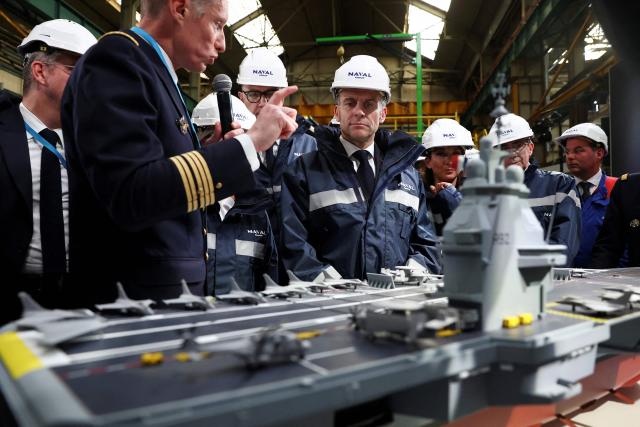 French President Emmanuel Macron looks at the model of a ship named "France Libre" as he gives a speech during a visit to the construction site of Naval Group Nantes-Indret, where the next generation French aircraft carrier is under construction, in Indret, western France, on March 18, 2026. The French president unveiled the name of France's next aircraft carrier: "France libre", as the country looks to reinforce its status as a major maritime power. Once completed, the new nuclear-powered flagship, which is set to replace the country's sole aircraft carrier, the Charles de Gaulle, will be the largest warship ever built in Europe. (Photo by Gonzalo Fuentes / POOL / AFP)