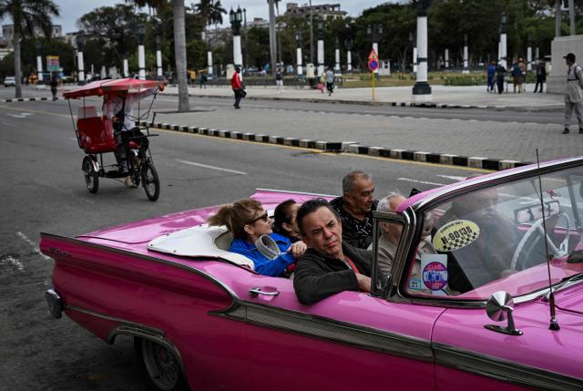 Tourists drive a classic American car down a street in Havana past a bike taxi on March 18, 2026. (Photo by YAMIL LAGE / AFP)