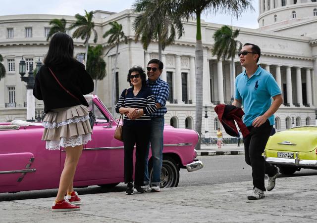 Tourists pose for photos with an American classic car in Havana on March 18, 2026. (Photo by YAMIL LAGE / AFP)