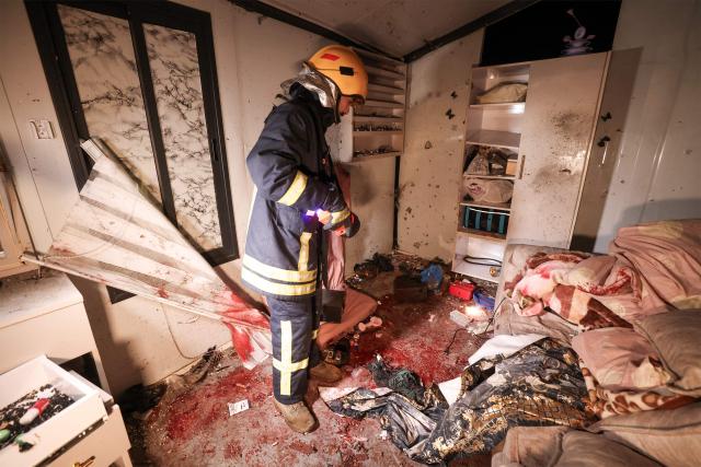 TOPSHOT - A Palestinian civil defence worker inspects the site where shrapnel from projectiles fell in Beit Awa near the Israeli-occupied West Bank city of Hebron on March 18, 2026. Four Palestinian women were killed in the occupied West Bank on March 18 by falling shrapnel, emergency responders said, shortly after Israel's military reported another Iranian missile barrage. The Palestinian Red Crescent confirmed four fatalities, all women, and six injuries ranging from moderate to minor, in the Beit Awa area near Hebron, marking the first Palestinian deaths in the ongoing Middle East war. (Photo by HAZEM BADER / AFP)