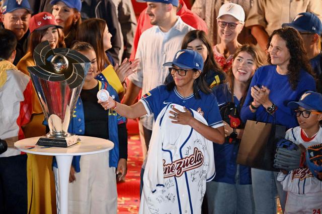 Venezuela's interim president Delcy Rodriguez holds a national baseball team jersey signed by all players next to the tournament trophy during an event to honor the national baseball team after its victory in the World Baseball Classic at the Miraflores Palace in Caracas on March 18, 2026. Venezuelan flags hang from windows, hundreds wear the national teams jersey, and a holiday has been declared: the country woke up celebrating on March 18 after its first World Baseball Classic title, a celebration that some even link to the fall of Nicolas Maduro. (Photo by Juan BARRETO / AFP)