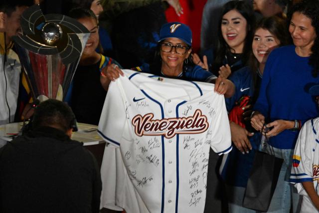 Venezuela's interim president Delcy Rodriguez holds a national baseball team jersey signed by all players next to the tournament trophy during an event to honor the national baseball team after its victory in the World Baseball Classic at the Miraflores Palace in Caracas on March 18, 2026. Venezuelan flags hang from windows, hundreds wear the national teams jersey, and a holiday has been declared: the country woke up celebrating on March 18 after its first World Baseball Classic title, a celebration that some even link to the fall of Nicolas Maduro. (Photo by Juan BARRETO / AFP)