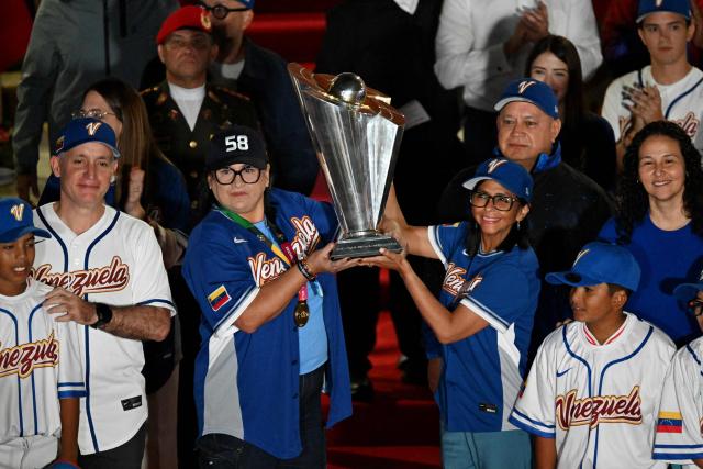 TOPSHOT - Venezuela’s interim President Delcy Rodriguez (R) and Aracelis Leon, president of the Venezuelan Baseball Federation, hold a trophy during an event to honor the national baseball team after its victory in the World Baseball Classic at the Miraflores Palace in Caracas on March 18, 2026. Venezuelan flags hang from windows, hundreds wear the national team’s jersey, and a holiday has been declared: the country woke up celebrating on March 18 after its first World Baseball Classic title, a celebration that some even link to the fall of Nicolas Maduro. (Photo by Juan BARRETO / AFP)