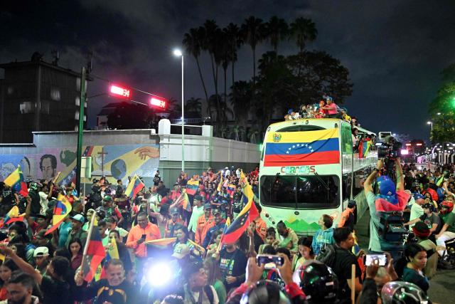 People carrying Venezuelan flags walk next to the bus transporting the tournament trophy during an event to honor the national baseball team after its victory in the World Baseball Classic in Caracas on March 18, 2026. Venezuelan flags hang from windows, hundreds wear the national team's jersey, and a holiday has been declared: the country woke up celebrating on March 18 after its first World Baseball Classic title, a celebration that some even link to the fall of Nicolas Maduro. (Photo by Juan BARRETO / AFP)