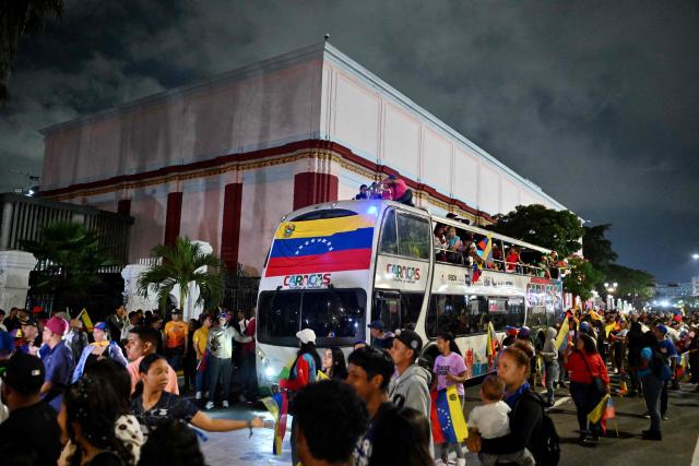 People carrying Venezuelan flags walk next to the bus transporting the tournament trophy during an event to honor the national baseball team after its victory in the World Baseball Classic in Caracas on March 18, 2026. Venezuelan flags hang from windows, hundreds wear the national team's jersey, and a holiday has been declared: the country woke up celebrating on March 18 after its first World Baseball Classic title, a celebration that some even link to the fall of Nicolas Maduro. (Photo by Juan BARRETO / AFP)