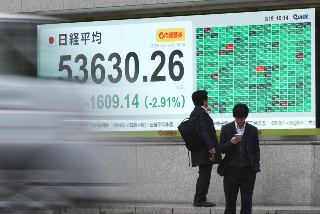 Pedestrians stand in front of an electronic quotation board displaying the Nikkei Stock Average on the Tokyo Stock Exchange along a street in Tokyo on March 19, 2026. (Photo by Kazuhiro NOGI / AFP)