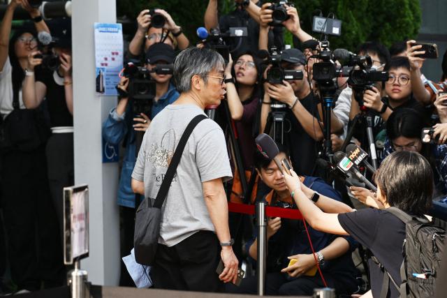 Journalists speak to a participant as he arrives to the public hearings into the Tai Po fire, one of the worst in Hong Kong's history, in Hong Kong on March 19, 2026. An independent committee investigating the devastating fire that ripped through a housing complex last year was starting a series of public hearings on March 19 into the blaze that killed 168 people. (Photo by Peter PARKS / AFP)