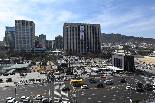 Workers set up the stage (R) for the comeback concert of K-pop boy group BTS at Gwanghwamun Square in Seoul on March 19, 2026. BTS, the world's biggest boy band, reunites on stage on March 21, in a K-pop extravaganza watched by hundreds of thousands of fans in downtown Seoul and by millions around the planet online. (Photo by Jung Yeon-je / AFP)