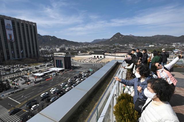 Workers set up the stage (centre L) for the comeback concert of K-pop boy group BTS in front of Gwanghwamun Gate (centre R), the main gate of Gyeongbokgung Palace, as visitors look from a rooftop viewing deck in Seoul on March 19, 2026. BTS, the world's biggest boy band, reunites on stage on March 21, in a K-pop extravaganza watched by hundreds of thousands of fans in downtown Seoul and by millions around the planet online. (Photo by Jung Yeon-je / AFP)