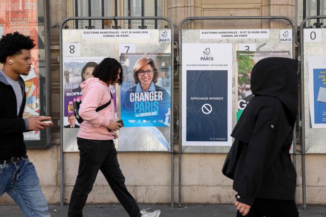 Pedestrians walk past campaign posters displayed in central Paris on March 19, 2026, ahead of the second round of France's municipal elections. (Photo by Charlotte SIEMON / AFP)